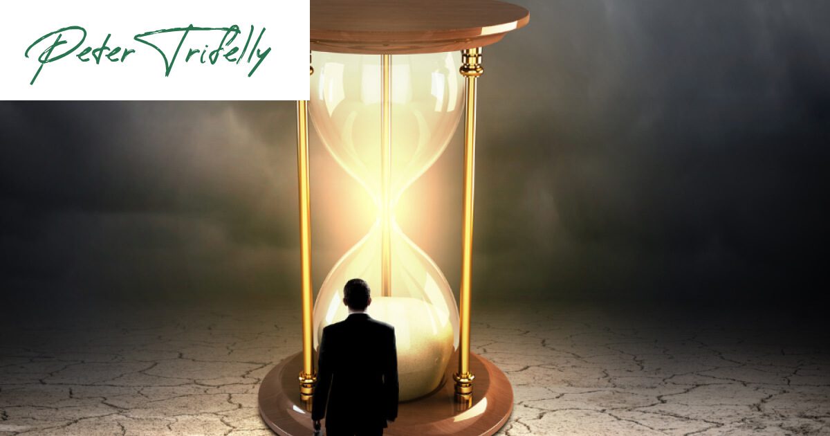 A man stands before a towering hourglass, symbolising the passage of time. What's your perspective of time?at Peter Trifelly Certified Business Coach